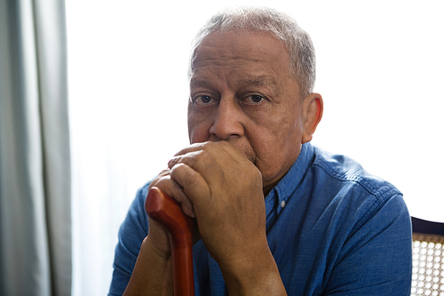 Portrait of sad senior man holding walking cane while sitting on chair in nursing home