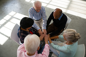 High angle view of senior friends stacking hands while sitting on chair in art class