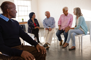 Senior man looking at friends talking while sitting on chair in art class