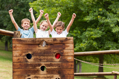 Kids standing with arms up on a playground ride in park on a sunny day