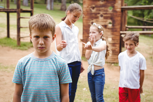 Upset boy with friends gossiping in background in park
