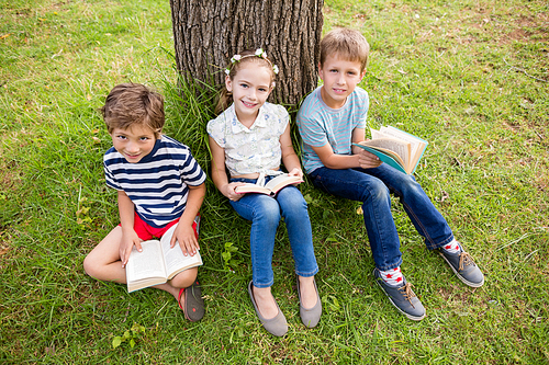 Kids sitting under tree and reading books in park on a sunny day