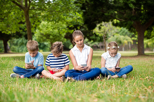 Kids using mobile phone in park on a sunny day