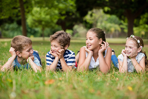 Happy children interacting with each other while lying on grass in park