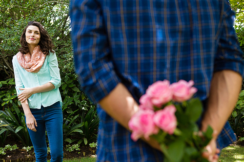 Mid-section of man hiding flowers behind back in garden