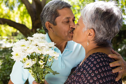 Senior man kissing while giving flowers to woman at the park