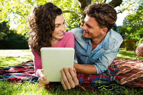 Couple lying on picnic blanket and using digital tablet in park