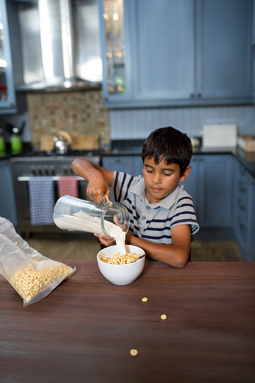 Boy pouring milk in cereals while having breakfast at home