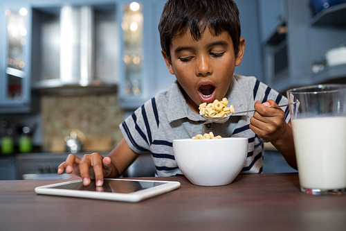 Close up of boy using tablet computer while having cereal breakfast at home