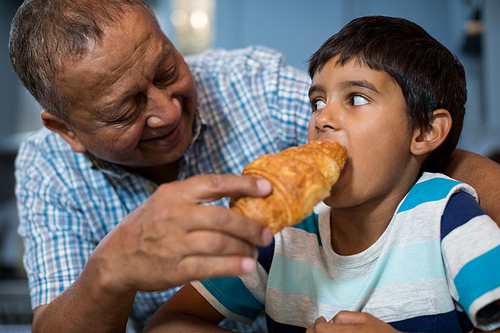 Grandfather feeding croissant to grandson while having breakfast