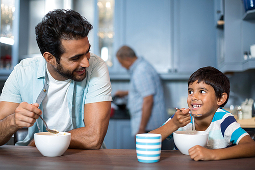 Father and son having breakfast at table with man in background