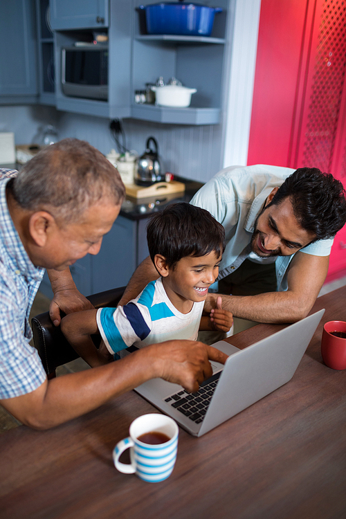 High angle view of happy father and grandfather looking at boy using laptop