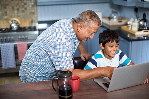 High angle view of grandfather assisting grandson using laptop in kitchen at home