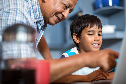 Close up grandfather assisting grandson using laptop in kitchen at home