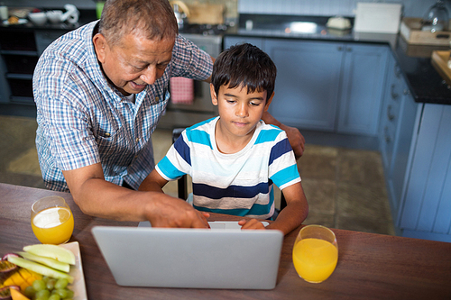 High angle view of smiling grandfather assisting grandson using laptop in kitchen at home