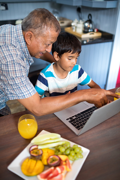 Grandfather assisting grandson using laptop in kitchen at home