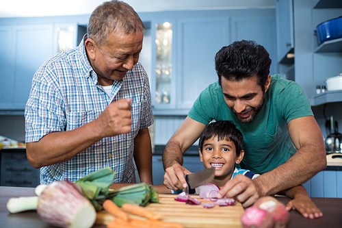 Man looking at boy cutting onion with father in kitchen at home