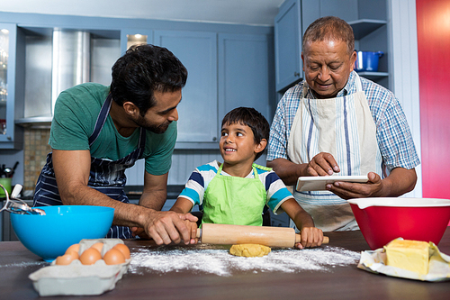 Man using table while standing by father and son preparing food in kitchen at home