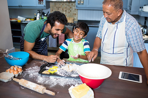 Boy preparing food while standing with father and grandfather in kitchen at home