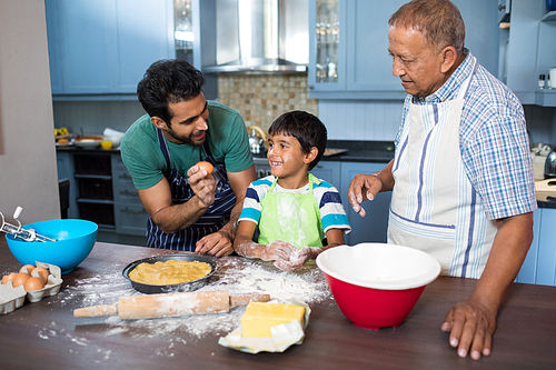 Man showing egg to boy standing by grandfather in kitchen at home