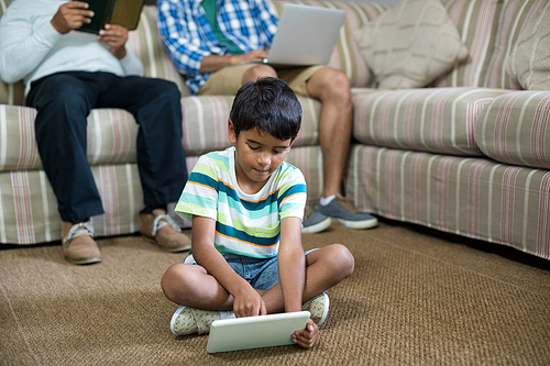 Boy using tablet with father and grandfather sitting on sofa in background