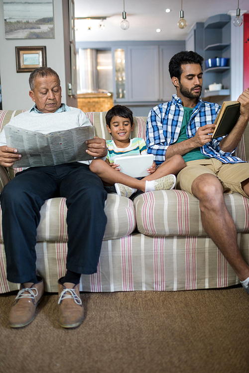 Boy with father and grandfather sitting on sofa in living room at home