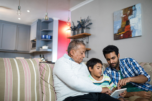 Father and grandfather pointing on tablet used by boy in living room at home