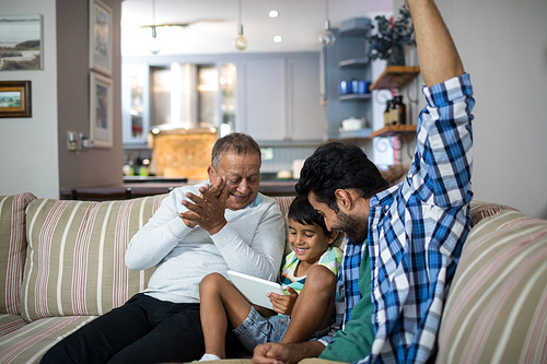 Happy grandfather and father with boy sitting on sofa in living room at home