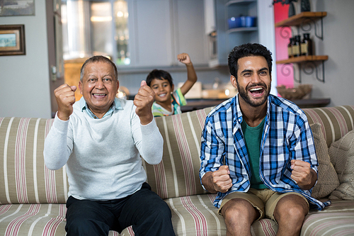 Cheerful family clenching fist while watching soccer match at home