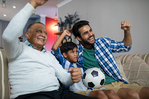 Happy family with arms raised watching soccer match while sitting on sofa at home