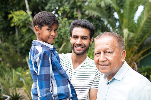 Portrait of father carrying son while standing by senior man at home