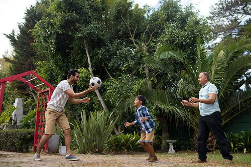 Happy family playing soccer against plant at park
