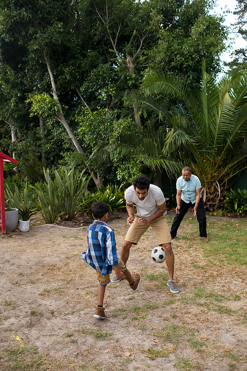 Boy playing soccer with parents on field in yard