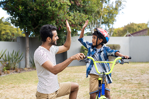Father and son doing high five while cycling in yard