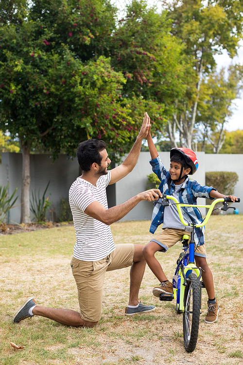 Full length of father and son doing high five while cycling in yard