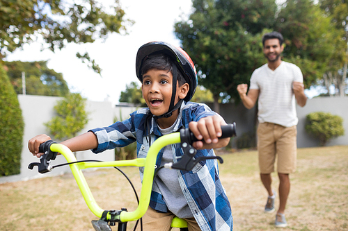 Boy cycling with father gesturing while standing in background