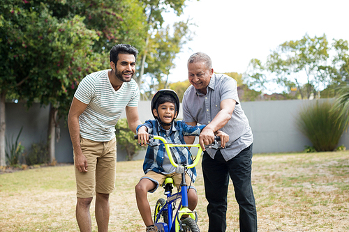 Father and grandfather assisting boy for riding bicycle while standing in yard