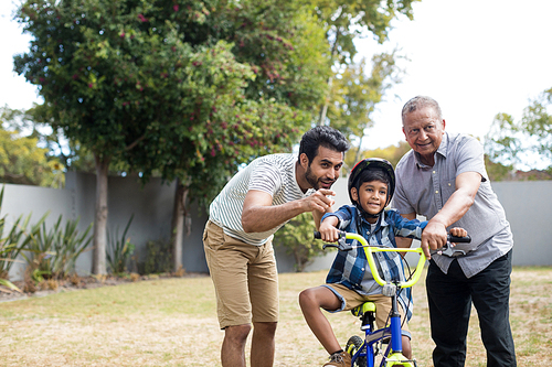 Boy learning bicycle with father and grandfather in yard