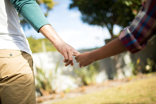 Cropped image of father and son holding hands while standing in yard