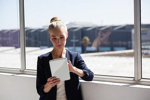 Smiling businesswoman using tablet while standing by window in office