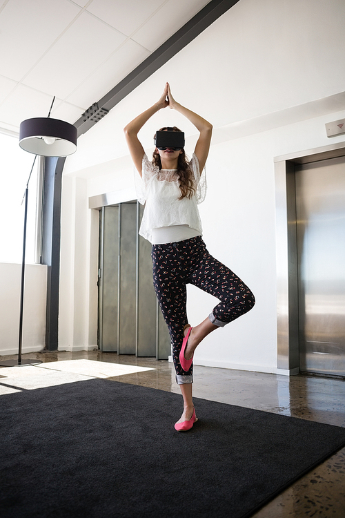 Businesswoman wearing virtual reality simulator practicing tree pose in office