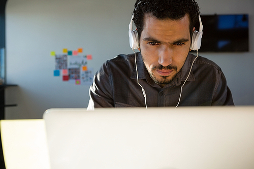 Young businessman listening to headphones while using laptop at office
