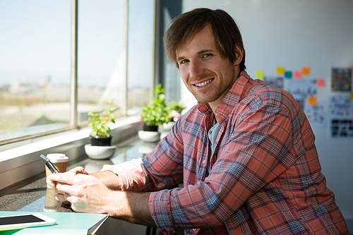 Portrait of smiling young man using phone by window at office
