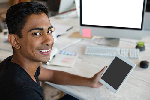 Portrait of smiling man holding digital tablet at desk in creative office