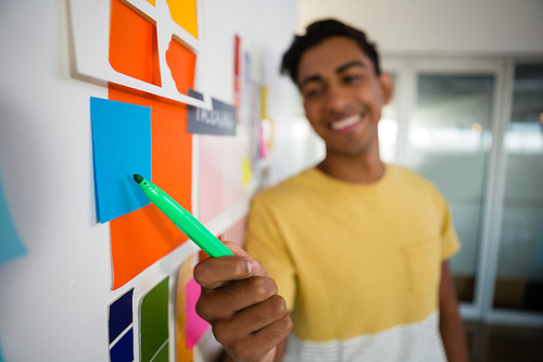 Smiling young man pointing at sticky notes with felt tip pen in creative office