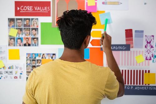 Rear view of young man pointing at sticky note in creative office