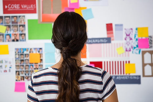 Rear view of businesswoman standing against sticky notes in creative office