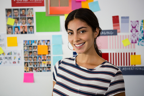 Portrait of beautiful woman standing against sticky notes in creative office