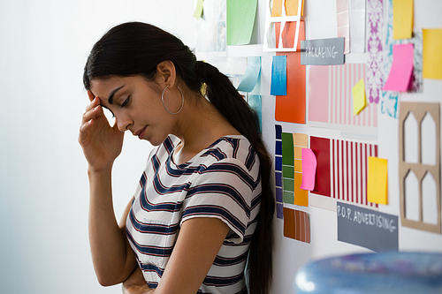 Tired young woman standing by sticky notes in creative office