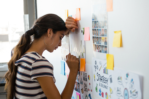 Tired young woman leaning on wall with sticky notes in creative office
